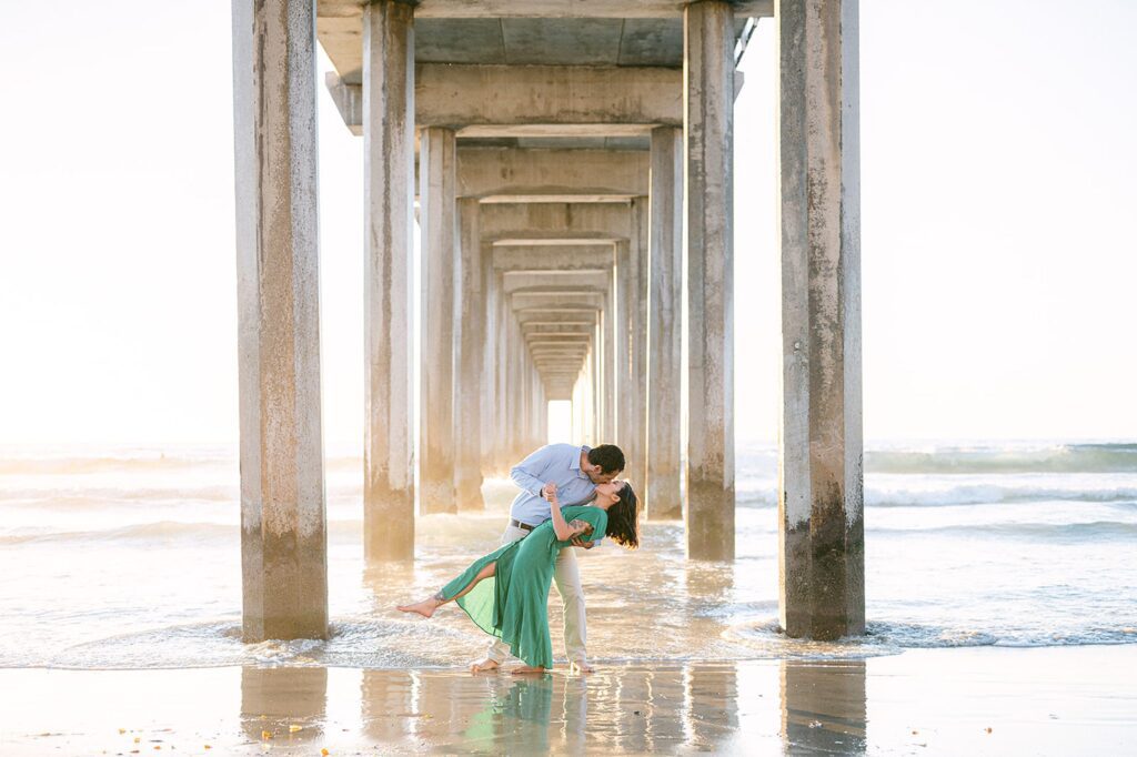 Golden Hour photo with groom dipping and kissing bride under the Scripps Pier